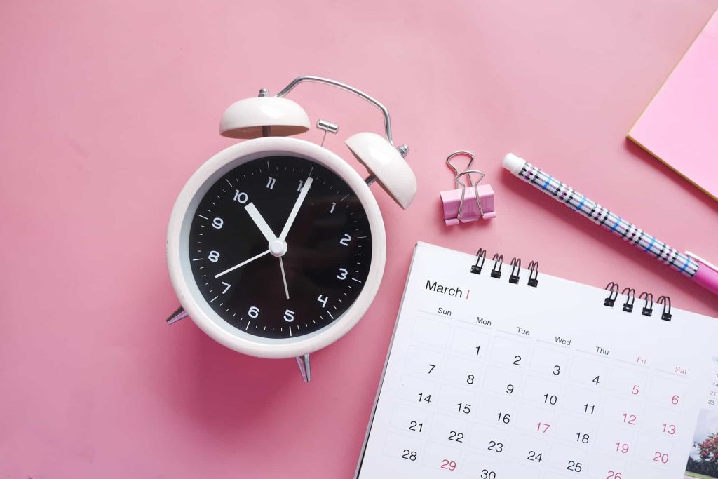 alarm-clock-beside-calender-in-pink-table