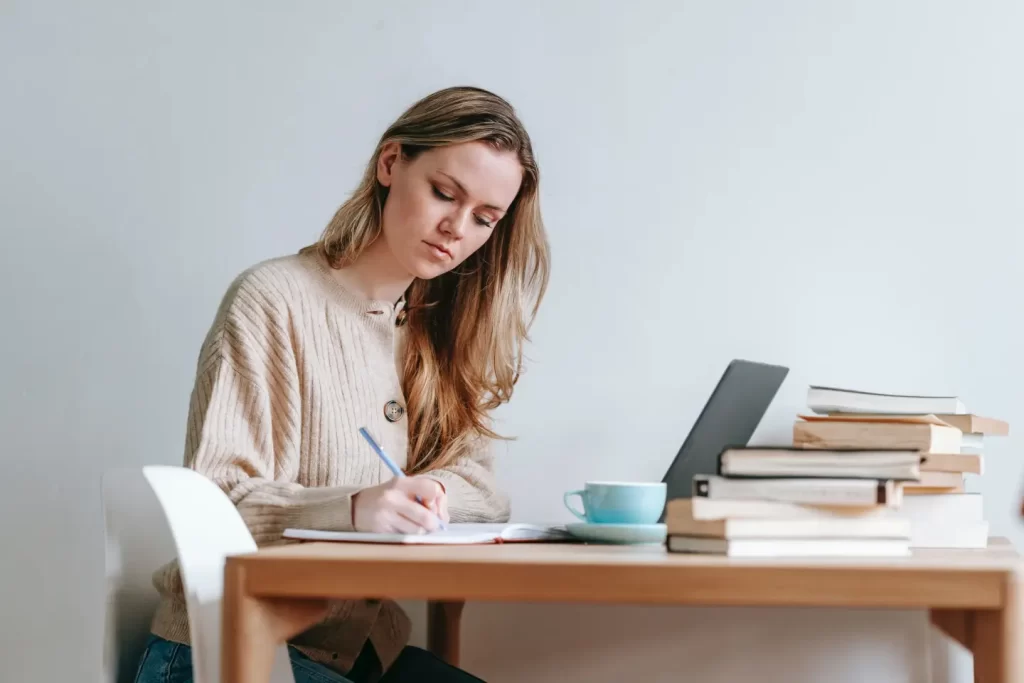 lady-taking-down-notes-beside-book-laptop