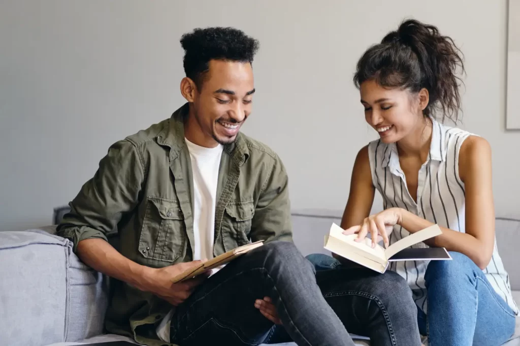 young-smiling-african-american-man-pretty-asian-woman-joyfully-reading-book-together-modern-co-working-space