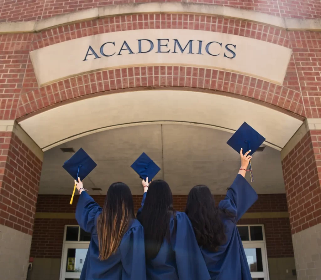 three-girls-in-graduation-gowns-hold-their-caps-in-the-air