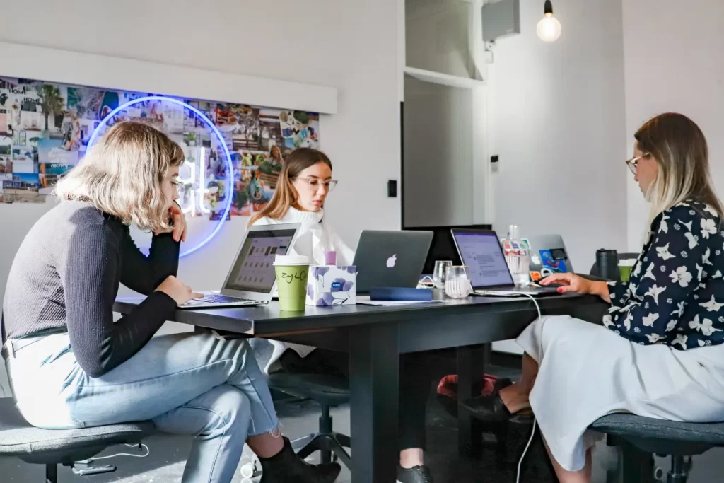 3-women-sitting-on-chair-in-front-of-table-with-laptop-computers