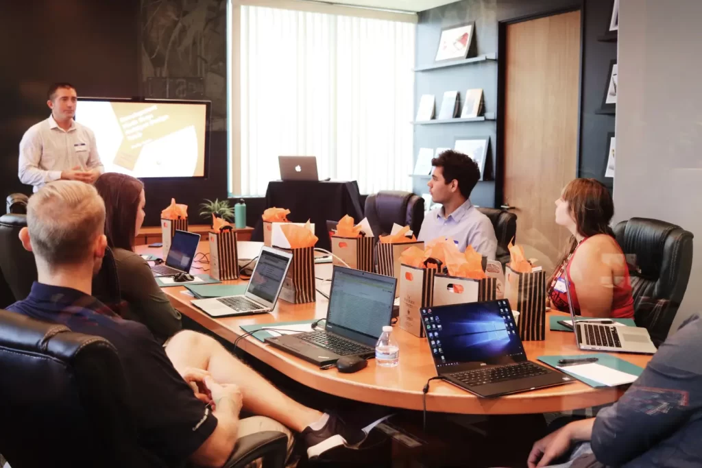 man-standing-in-front-of-people-sitting-beside-table-with-laptop-computers